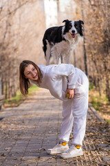 Black and white border collie dog stands on the back of the mistress on a walk in the autumn park. 