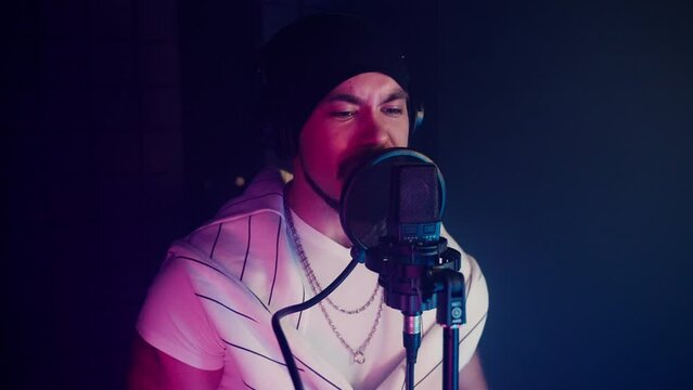 portrait of handsome man singing and doing rap song in isolation booth of modern recording studio