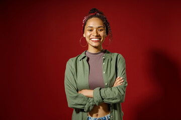 Portrait of charming smiling woman looks camera with crossed hands on red studio background