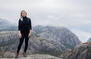 a girl with a backpack standing on the rock in the mountains on a hike in Norway on fjord