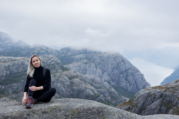 a girl with a backpack sitting on the rock in the mountains on a hike in Norway on fjord