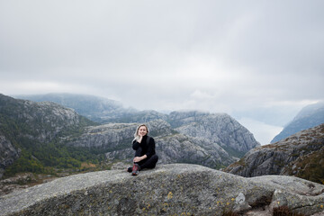 a girl with a backpack sitting on the rock in the mountains on a hike in Norway on fjord