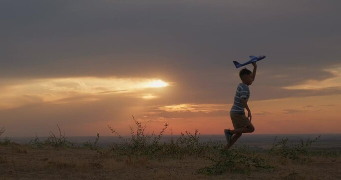 Silhouette view of little boy running with a toy airplane at sunset. Kid dream. Silhouette shot