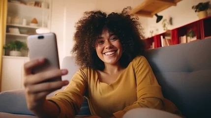 Fotobehang Happy afro American woman relaxing on the sofa at home, Smiling girl taking selfie picture with smartphone lying on the couch. © Pro Hi-Res