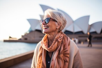 Lifestyle portrait photography of a pleased woman in her 60s that is wearing a chic cardigan at the Sydney Opera House in Sydney Australia
