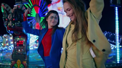 Happy girls dancing city amusement park at night. Cheerful girlfriends holding