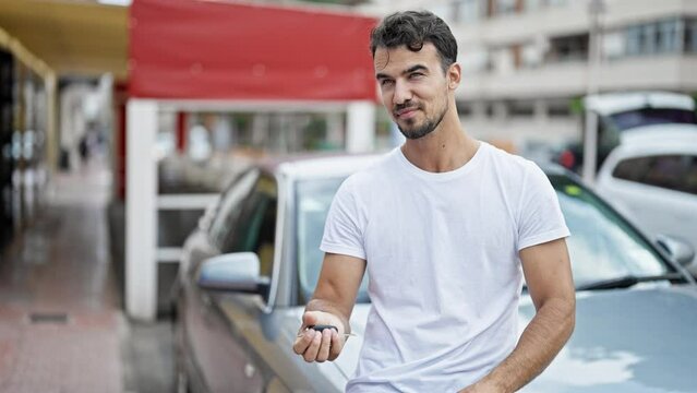 Young hispanic man holding key of new car doing thumb up gesture at street