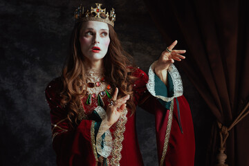 medieval queen in red dress with white makeup and crown