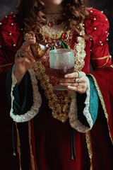 Medieval queen in red dress pouring poison into goblet