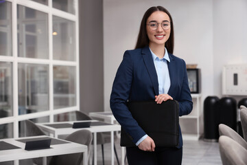 Happy real estate agent with leather portfolio indoors. Space for text