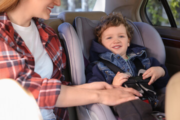 Mother fastening her son in child safety seat inside car