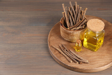 Dried sticks of licorice roots and essential oil on wooden table. Space for text