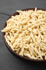 Uncooked trofie pasta in bowl on grey wooden table, closeup