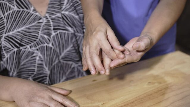 Caregiver massaging finger of elderly woman in painful swollen hand due Cancer chemotherapy .