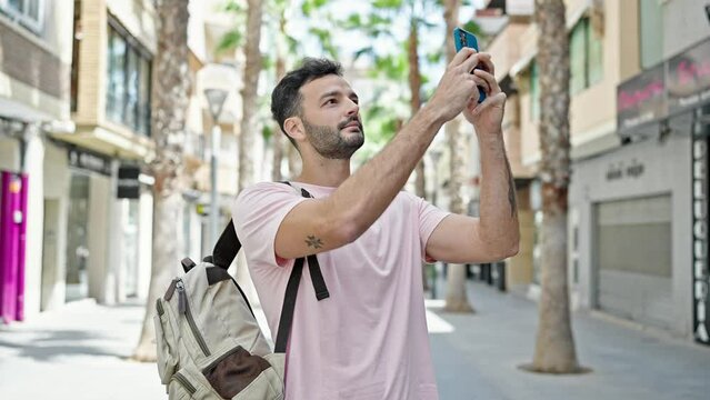 Young hispanic man recording video by smartphone wearing backpack at street
