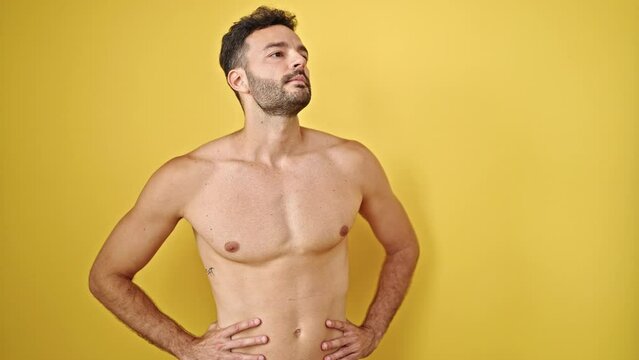 Young hispanic man tourist standing shirtless with serious face over isolated yellow background