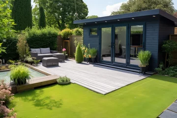 Tuinposter view of a back garden with artificial grass, grey paving slab patio, summer house garden timber outbuilding, fish pond © Kien