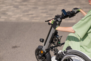 A woman controls a wheelchair using a special manual device. Close-up of female hands on electric handbike. 