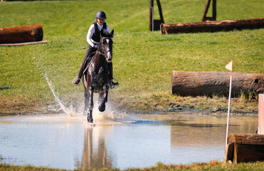Horse with rider in an eventing tournament galloping through the water to the next jump..