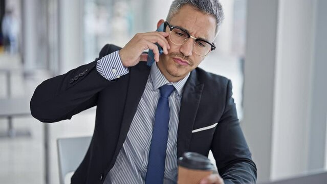 Young hispanic man business worker talking on smartphone holding coffee at office
