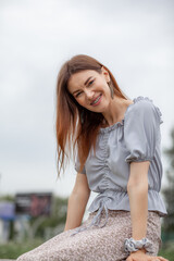 Smile of a young and beautiful girl with braces on her white teeth. A girl with long hair and a dress poses in the park. Straightening crooked teeth using a braces system.