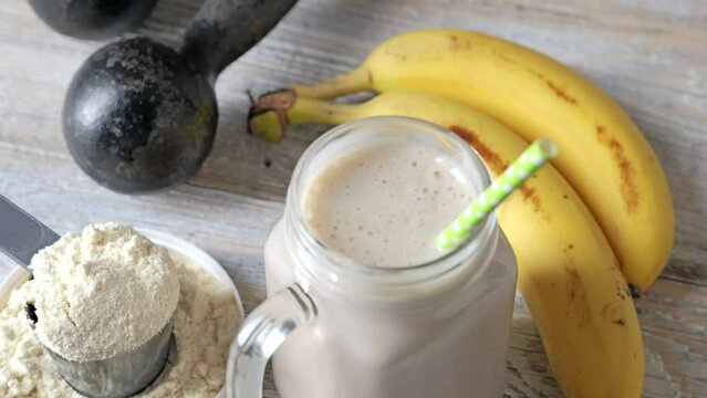 Protein drink, banana fruits, and dumbbells on a wooden background. Healthy eating and fitness concept.