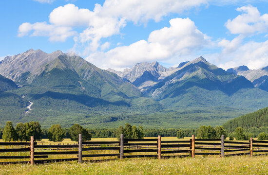 Scenic mountain landscape with hay meadow and rocky ridge of mountains against blue sky with clouds on sunny August day.  Eastern Sayan Mountains, Tunka foothill valley, Buryatia, Siberia