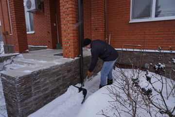 A man cleans snow in the winter in the courtyard of the house.