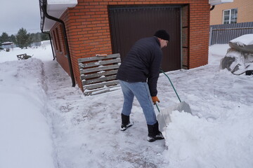 A man cleans snow in the winter in the courtyard of the house.