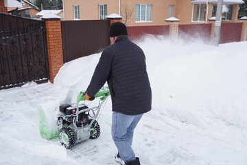 A man cleans snow in the winter in the courtyard of the house,  man cleaning snow with a snow blower