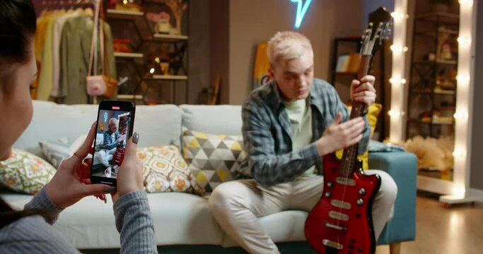 Guitarist reviewer blogger records video about pros and qualities of electric guitar describing ease of use. Man praises admires guitar record video for social networks. Female hands holds smartphone