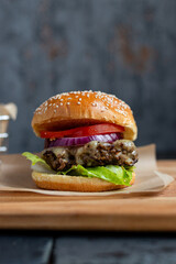 Beef cheese burger stacked in a seeded bun with lettuce, tomato, onion and cheddar cheese. 