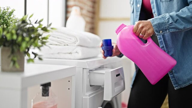 Young beautiful hispanic woman pouring detergent on washing machine at laundry room