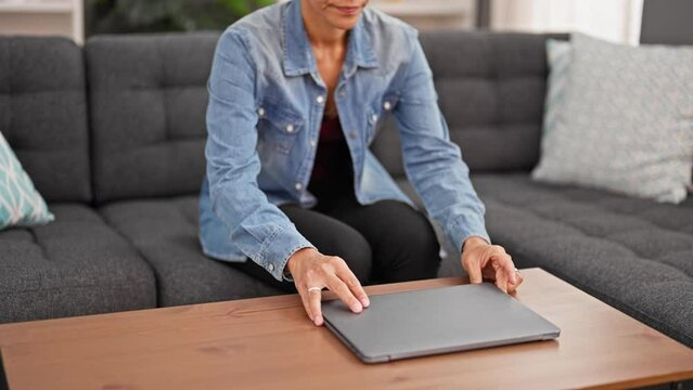 Young beautiful hispanic woman sitting on sofa opening laptop to use at home