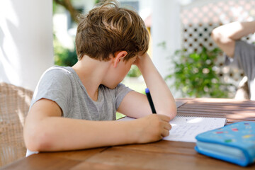 Hard-working sad school kid boy making school homework . Upset tired child and learning concept
