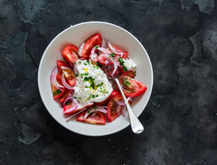Salad with fresh fragrant tomatoes, burrata, red onion and pesto sauce on a dark background, top view