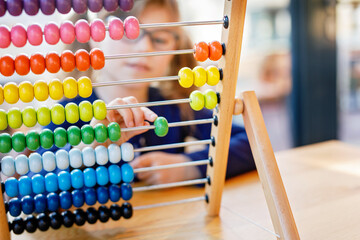 Little preschool girl playing with educational wooden rainbow toy counter abacus. Healthy happy child with glasses learning to count and colors, indoors on sunny day.