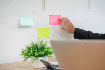Serious businessman managing project tasks on sticky notes writes start-up business ideas using colorful Post-it stickers, plans corporate strategy board. Creative priority to-do list concept.