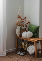 Cozy autumn interior of the hallway - an oak bench with a basket with blankets, pillows, branches, pumpkin, slippers on a jute rug