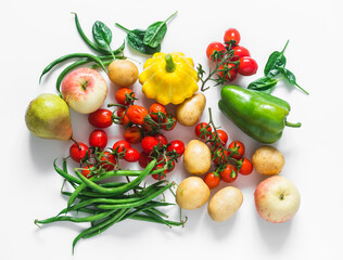 A variety of seasonal vegetables and fruits on a white background - cherry tomatoes, potatoes, string beans, squash, pear, apple