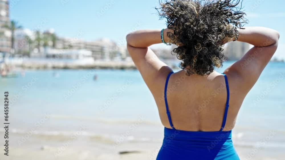 Canvas Prints Young beautiful latin woman tourist wearing swimsuit combing hair with hands at beach