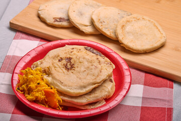 Savor the rich flavors of El Salvador with pupusas, a traditional Central American dish, served with curtido and savory sauce on a rustic wooden board