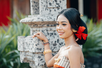 Obraz premium Smiling girl in a vivid sari, standing calmly in a vine-covered temple in Indonesia.