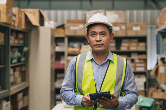 Portrait senior engineer happy working inventory manager. Southeast Asian adult male worker standing in factory store warehouse.