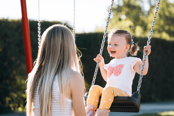 a young mother and her little daughter ride on a swing in the park and are very happy