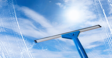 Rubber squeegee cleans a soaped window and clears a stripe of bright blue sky, spring cleaning...
