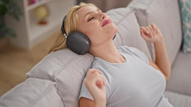 Young blonde woman listening to music relaxed on sofa at home