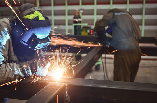 Builder welder in a safety helmet welding a steel structure at a construction site