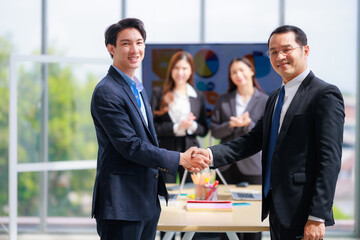 Two Asian Business Professionals Shaking Hands in Office, Celebrating a Successful Corporate Agreement