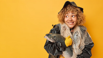 Delighted curly haired woman proudly carries massive salmon er beaming smile revealing joy of...